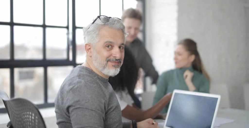 cheerful-male-worker-sitting-with-laptop-and-multiethnic-3865577-scaled-e1590093024159